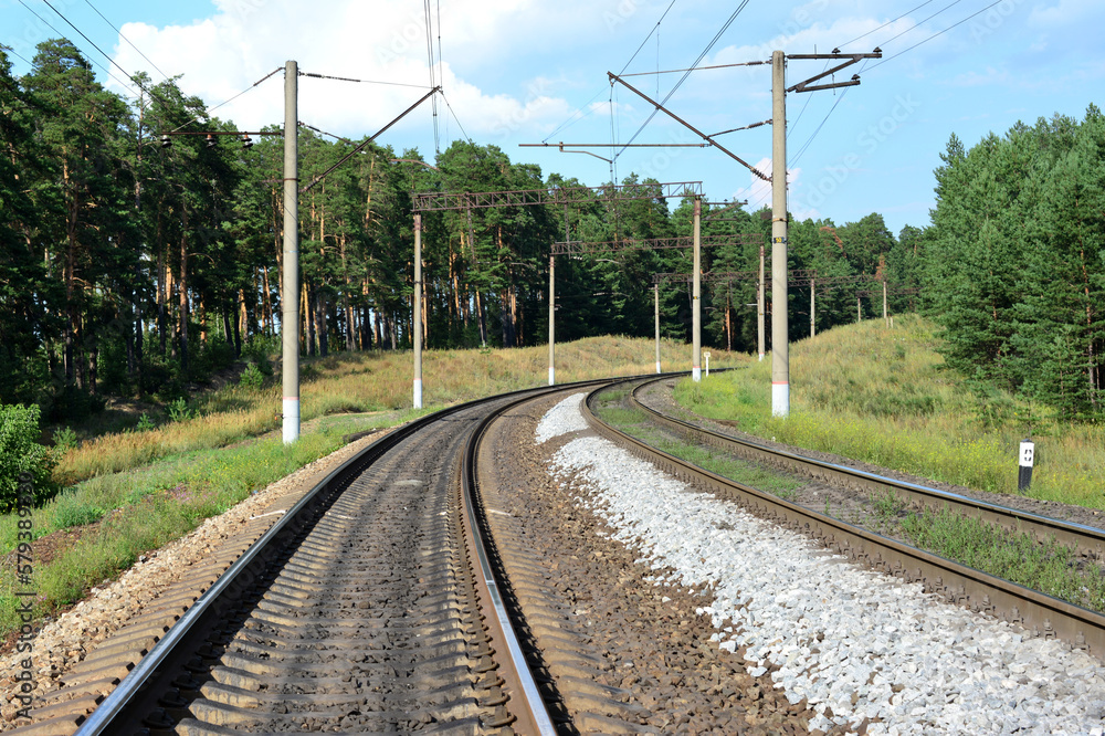 A railway with a line of electric columns and trees along in the background A railway with a line of electric columns and trees along in the background