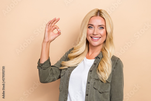 Photo of positive pretty lady wear khaki denim clothes hand okey symbol empty space isolated on beige color background