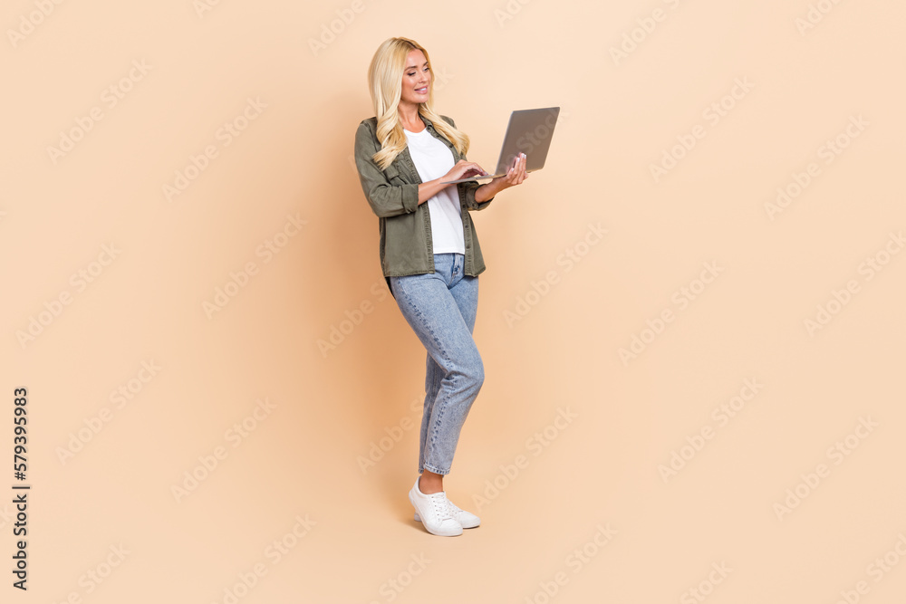Full length photo of adorable stunning lady wear stylish clothes use macbook netbook write email isolated on beige color background Full length photo of adorable stunning lady wear stylish clothes use macbook netbook write email isolated on beige color background