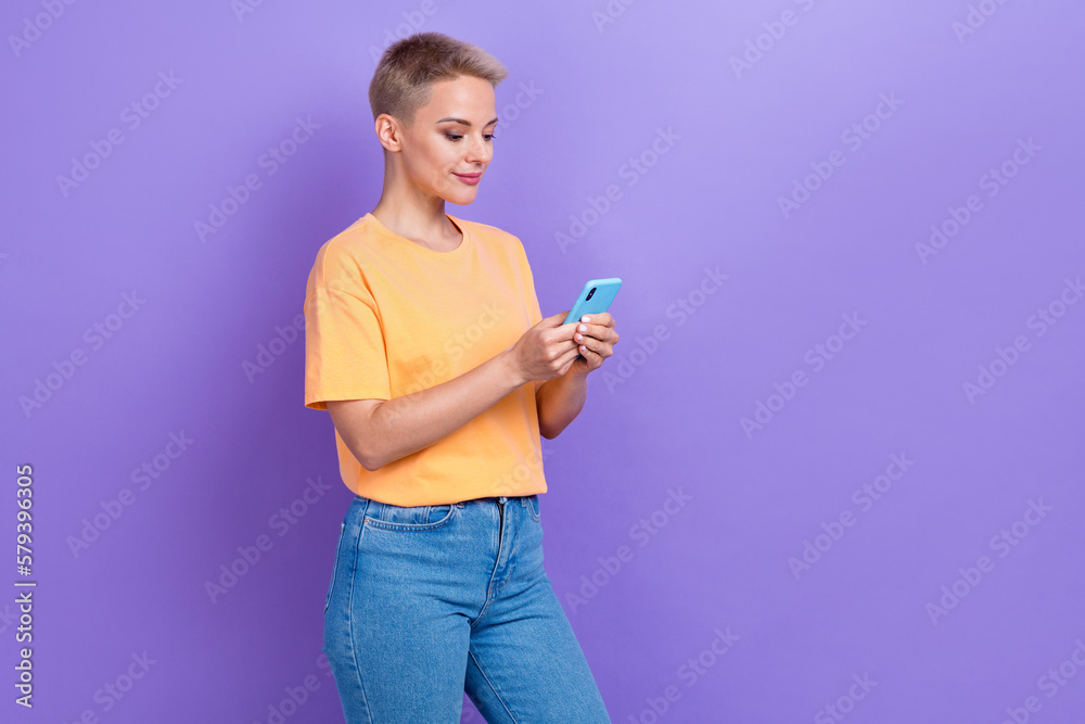 Photo of positive blogger attractive girl wear orange t-shirt denim jeans hold phone communicating new app chat isolated on violet color background Photo of positive blogger attractive girl wear orange t-shirt denim jeans hold phone communicating new app chat isolated on violet color background