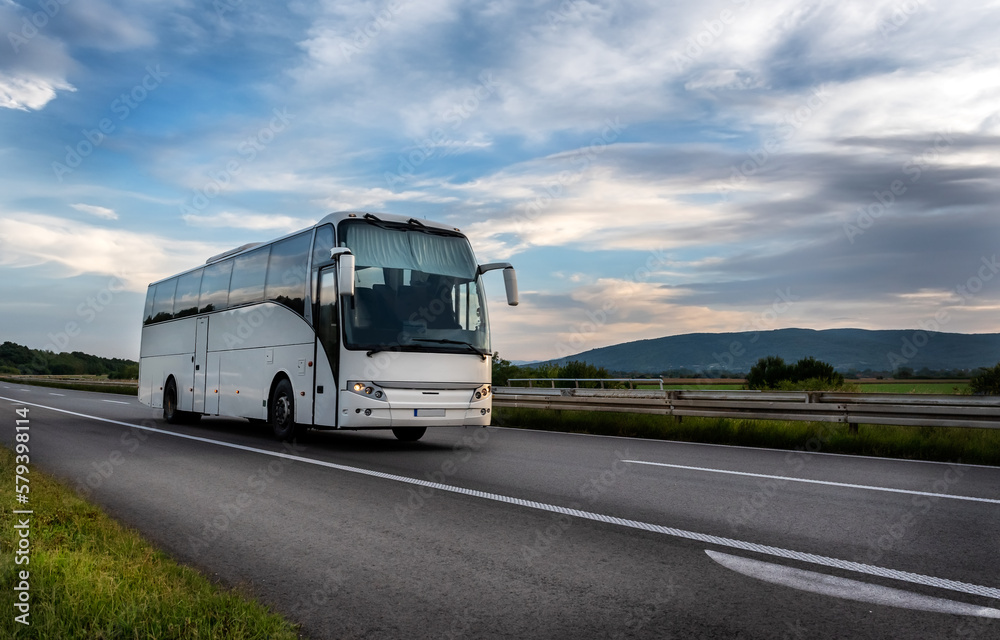 White Modern comfortable tourist bus driving through highway at bright sunny sunset. Travel and coach tourism concept. Trip and journey by vehicle