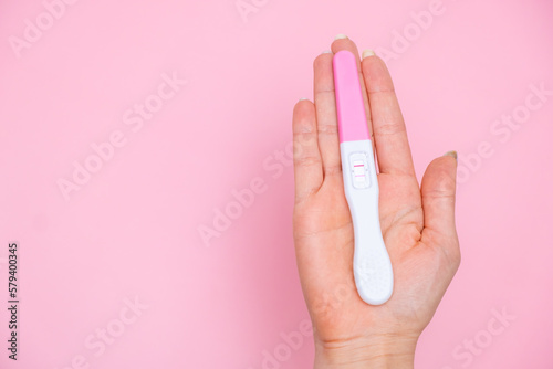 Female hand holding a positive pregnancy test on the pink background. Planning of pregnancy and motherhood concept with copy space 