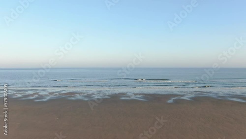 langsamer Drohnenflug über den Strand auf das blaue Meer hinaus mit leichten Wellen und klarem Himmel photo