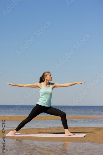 Virabhadrasana, woman in sportswear do sports fitness and yoga on seashore. athletic millennial female trains before marathon, healthy lifestyle, love for her body, mental and physical condition, 
