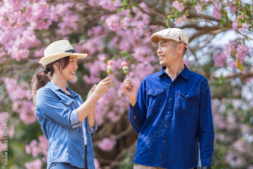 Young asian couple celebrating the sweet hanami dango dessert while walking in the park at cherry blossom tree during spring sakura festival with copy space