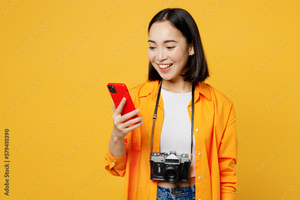 Young smiling woman wear summer casual clothes hold use mobile cell phone isolated on plain yellow background. Tourist travel abroad in free spare time rest getaway. Air flight trip journey concept. Young smiling woman wear summer casual clothes hold use mobile cell phone isolated on plain yellow background. Tourist travel abroad in free spare time rest getaway. Air flight trip journey concept.