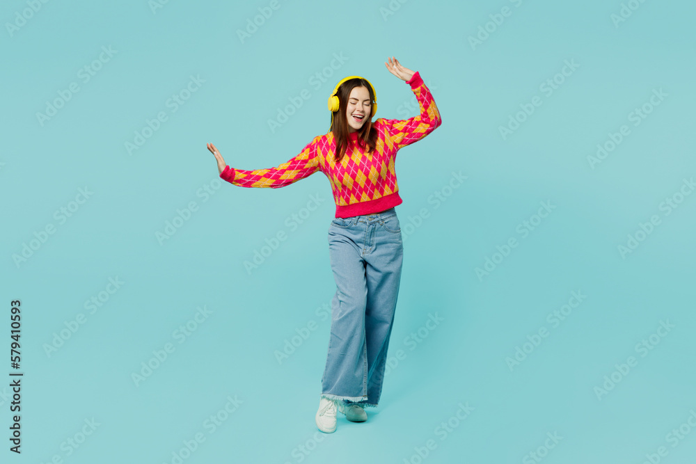 Full body young happy woman wear bright casual clothes headphones listen to music dance raise up hands gesticulating arms isolated on plain pastel light blue cyan background studio. Lifestyle concept. Full body young happy woman wear bright casual clothes headphones listen to music dance raise up hands gesticulating arms isolated on plain pastel light blue cyan background studio. Lifestyle concept.
