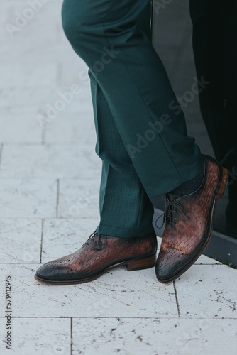 Vertical shot of a stylish man in dark gray suit pants and textured leather oxford shoes
