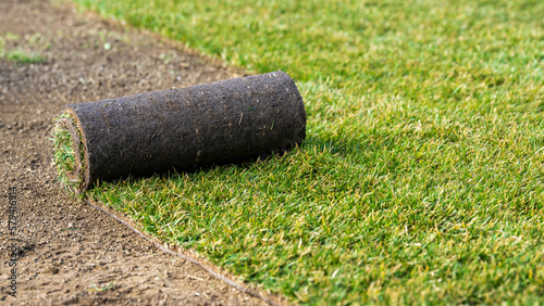 Roll of new turf beeing rolled out in the garden in spring time - rolled grass fresh from field