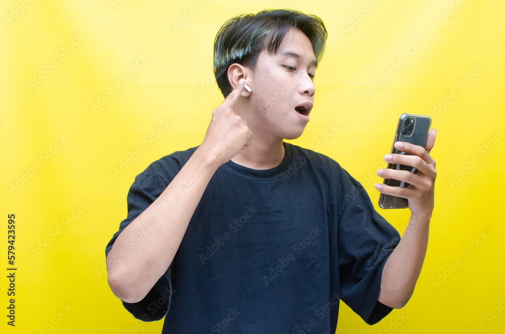 An enthusiastic Asian man with peek-a-boo hair is using airpods while dancing joyfully, checking his phone, and listening to music. An enthusiastic Asian man with peek-a-boo hair is using airpods while dancing joyfully, checking his phone, and listening to music.