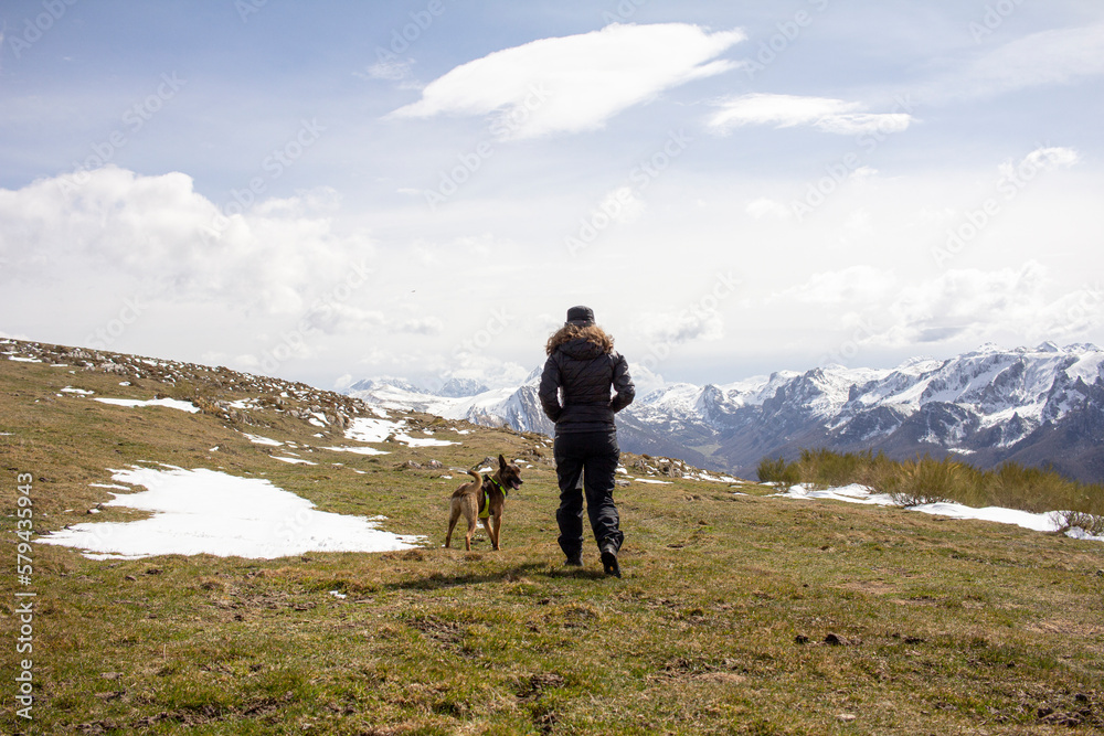 woman walking with her dog through the mountains of Somiedo, Asturias in winter, with the Picos de Europa in the background