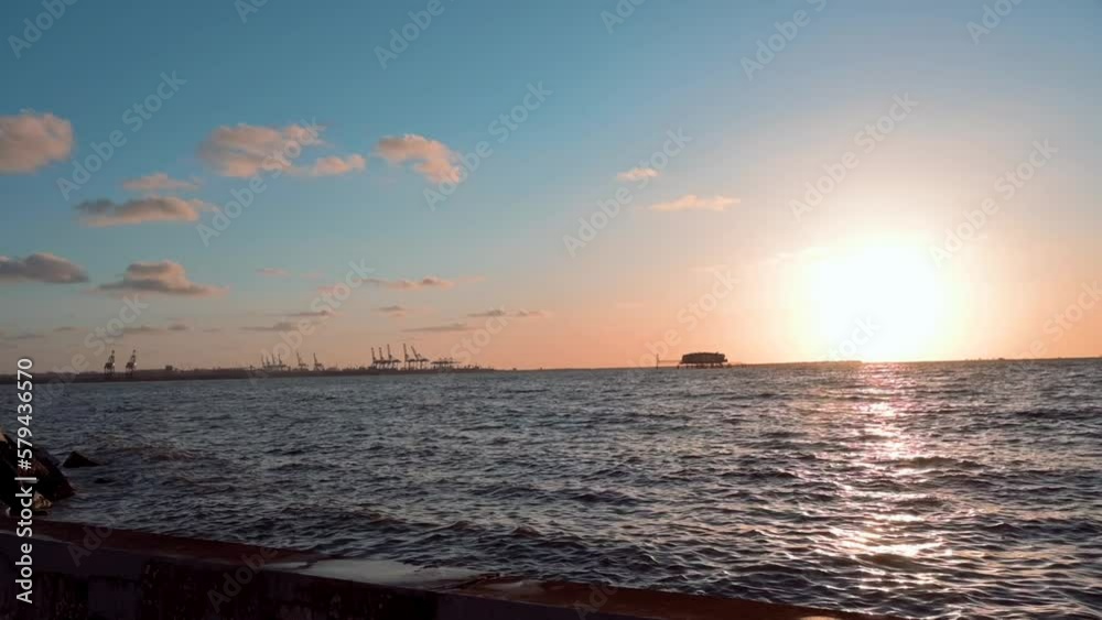 Slow motion of the calm Mediterranean Sea with the golden sunset and a ship port in the background Slow motion of the calm Mediterranean Sea with the golden sunset and a ship port in the background