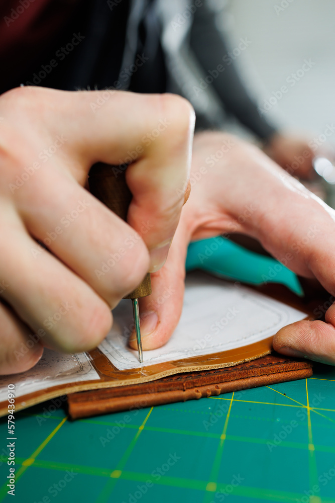 Obraz premium A man's hand holds pieces of leather for a leather wallet in his workshop. The process of working with natural brown leather. The craftsman holds the craft
