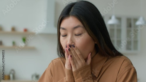 Unhealthy sick Asian woman girl sneeze cover face with hands in kitchen Japanese businesswoman suffer runny nose has allergy covid-19 symptom fever flu Korean lady feeling bad sneezing cold at home