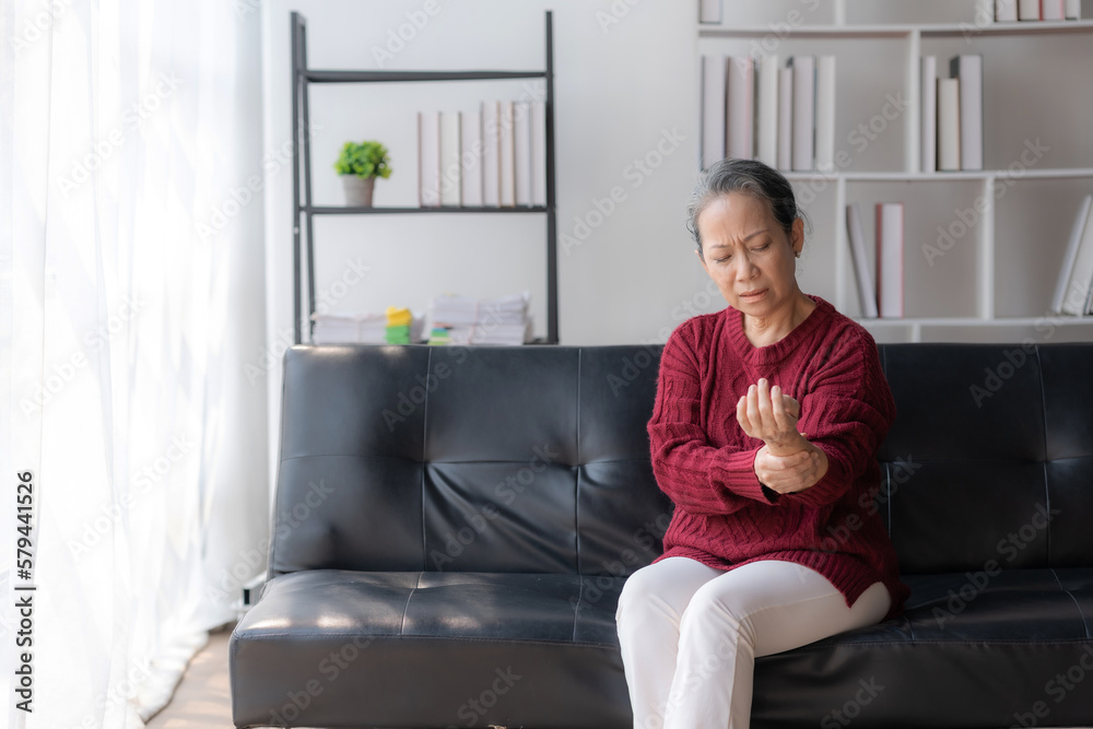 Asian old woman with body aches, leg pain, bone pain, stiff muscles, arm pain, hand pain, sitting on the sofa in the living room stretching to relax. Asian old woman with body aches, leg pain, bone pain, stiff muscles, arm pain, hand pain, sitting on the sofa in the living room stretching to relax.