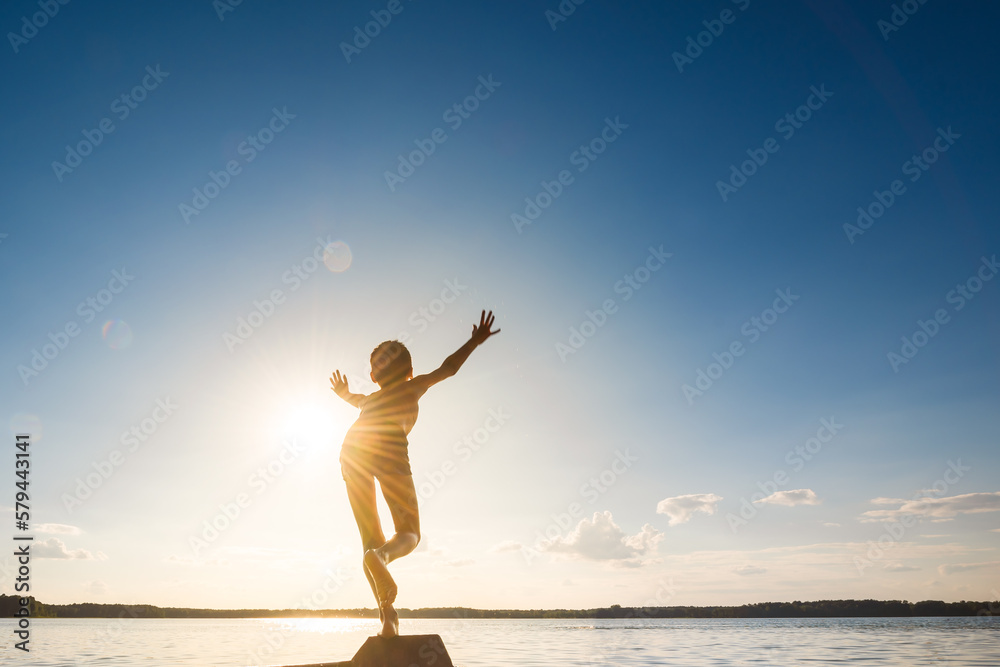 Child boy stretches his hand to the sun in blue sky. Kid jumps into water. Hello sunny summer concept. Space for text.