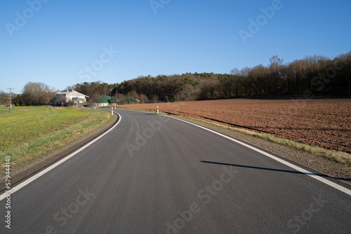 Asphalt road between grass and arable land with blue sunny sky in spring