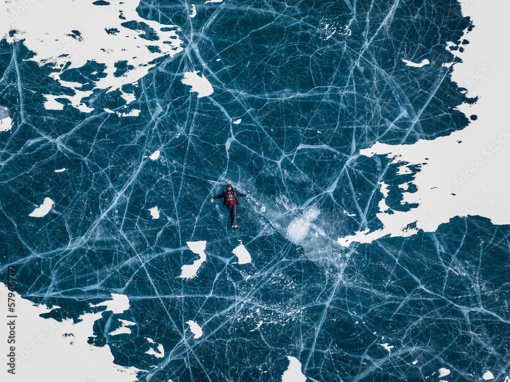 aerial view of a man with beard in sweater and in ice skates lying on blue ice of abraham lake in jasper and banff national park