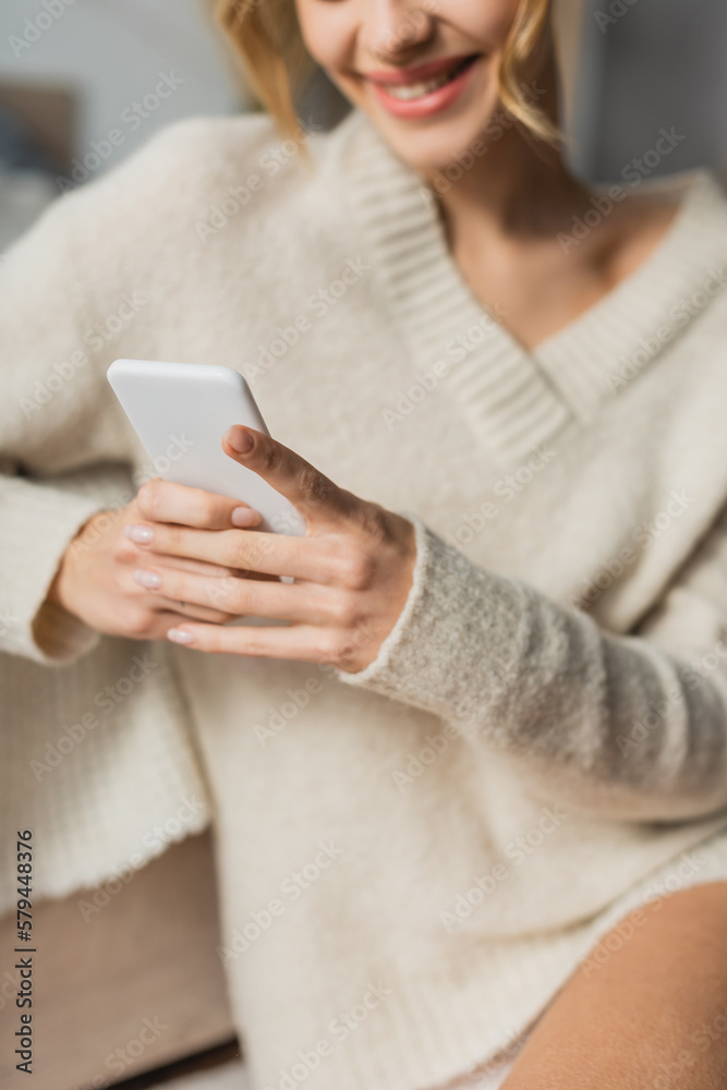cropped view of happy woman in knitted sweater chatting on smartphone at home. cropped view of happy woman in knitted sweater chatting on smartphone at home.