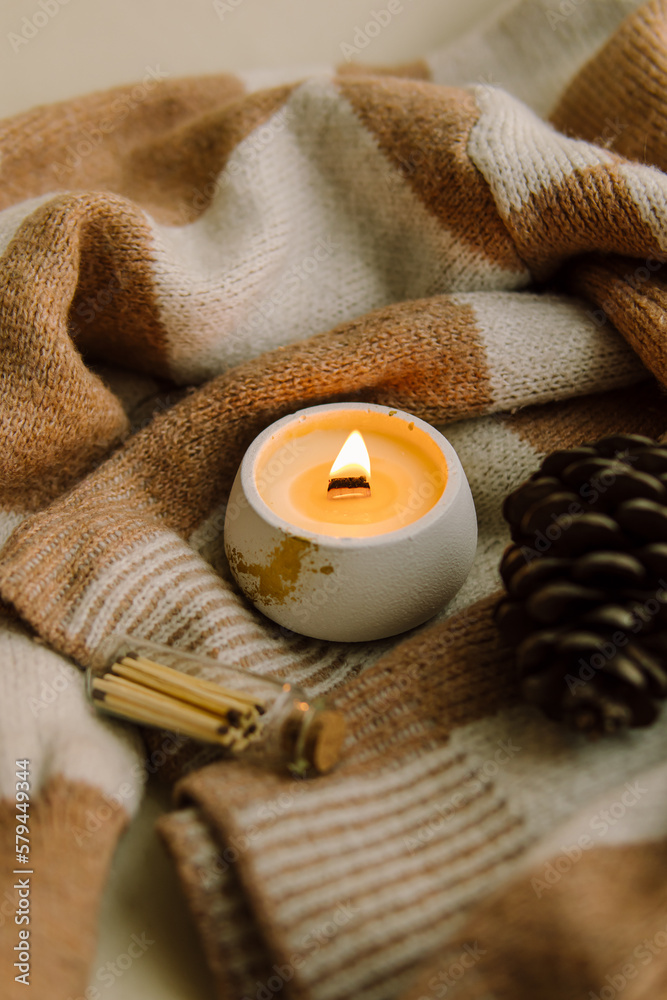 Interior candle in a plaster candlestick, wooden matches and pine cone. Natural. Handmade candle on brown knitted sweater Interior candle in a plaster candlestick, wooden matches and pine cone. Natural. Handmade candle on brown knitted sweater