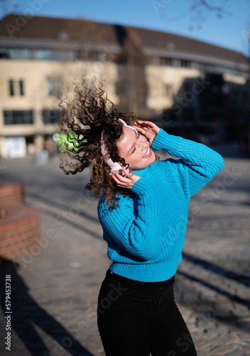 Young fashion woman with headphones listening to music and dancing outdoors