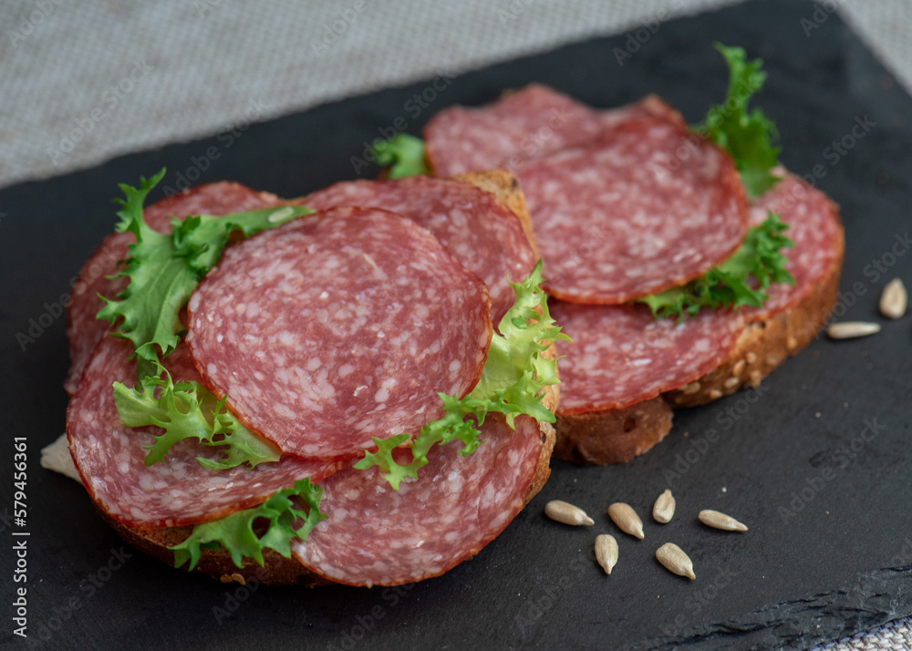 sliced salami and lettuce on black background, top view. open sandwiches with sliced salami sausage on rye bread sliced salami and lettuce on black background, top view. open sandwiches with sliced salami sausage on rye bread