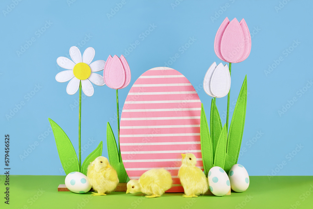 Felt spring flowers and wooden Easter egg with chicks in front of blue background