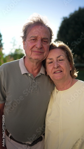 A happy married older couple looking at camera at park with during sunny day backlight. Close up of senior faces of 70s husband and wife in Vertical Video