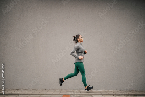 Full length of a fit female runner running on the street.