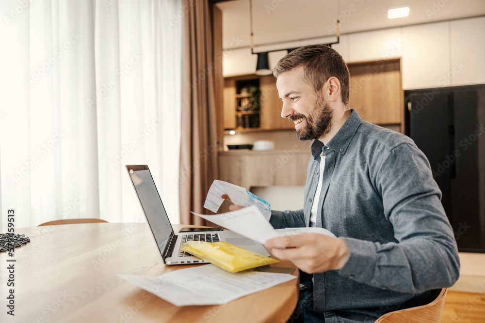 A happy man is holding bills in his hands and preparing for online payment. A happy man is holding bills in his hands and preparing for online payment.