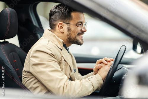 A young happy businessman is waiting in traffic while driving his car.