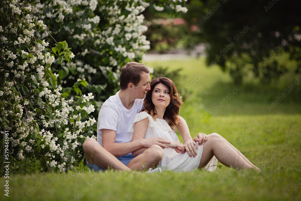 Young man and woman couple in a blooming garden near jasmine bush. Tender holding each other. Spring lovestory. Brown-haired girl with long hairs with her boyfriend or husband. Young couple on a date Young man and woman couple in a blooming garden near jasmine bush. Tender holding each other. Spring lovestory. Brown-haired girl with long hairs with her boyfriend or husband. Young couple on a date