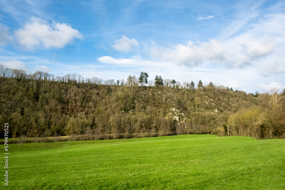Green meadow turning into hill on which trees grow. Blue sky with small clouds. Rural landscape in France. Green meadow turning into hill on which trees grow. Blue sky with small clouds. Rural landscape in France.