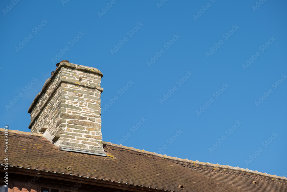 Stone chimney and part of roof made of tiles of old house against blue clear sky.