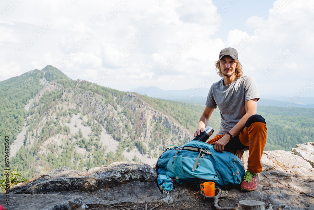 Packing a backpack on a hike, putting equipment in a bag, a camping kit for survival in the forest, a guy climber resting on a mountain, a man trekking a rock.