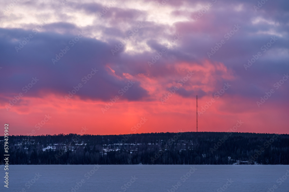 Red and purple sky over the frozen lake after the sunset in Finland with radio tower in the distance.