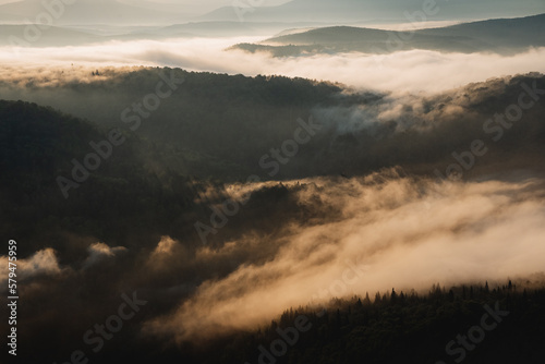 Morning fog spreads over the tops of the forest, dawn in the mountains, the morning sun illuminates the treetops, the haze below in the valley of the hills.
