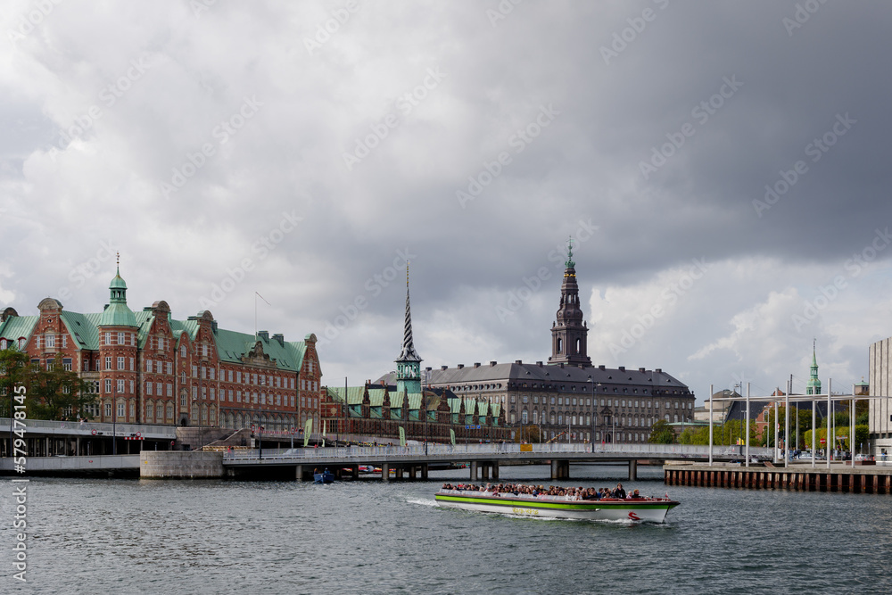 Outdoor top view over canal and tour boat and background of Børsen, waterfront building with a striking spire and Christiansborg Palace. 