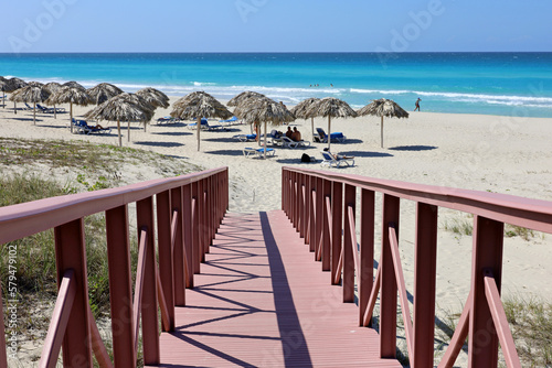 Canvas Print Stairs to tropical beach with white sand, wicker parasols and tanning people