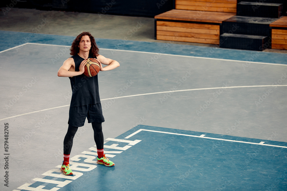 Sports guy on the basketball court, a guy with long hair trains with the ball on the basketball court, streetball.