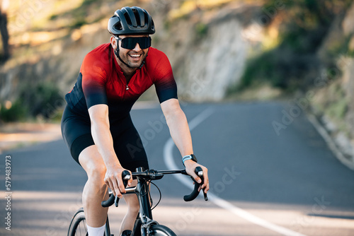 Young male cyclist smiling while riding a road bike on a hill