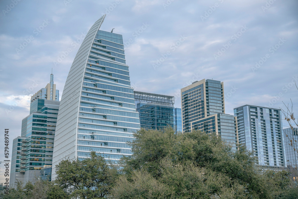 Buildings with modern architecture designs against cloudy sky in Austin Texas. Views from Butler Metro Park of the city skyline amidst vast skyscape and lush foliage.