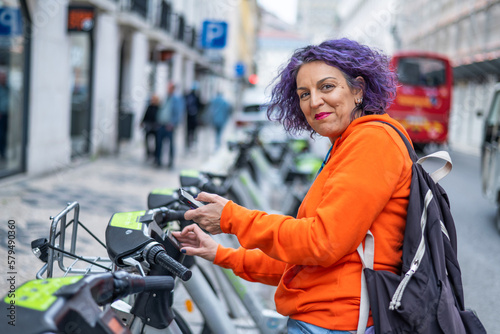 Mature Woman With Phone And Electric Bike Instead Of Transportation, Clean Energy Or Sustainable Travel. Technology, Electric Bicycle And Respectful With The Environment. Lifestyle