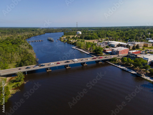 Aerial shot of highway bridge and swing bridge over the wide river at Milton, Florida. Land area with trees on left and buildings on the right connected by two bridges over the river.