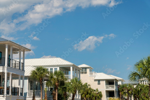Row of houses in Destin, Florida with balconies and palm trees outdoors. Houses exterior with painted light colors against the sky with clouds.