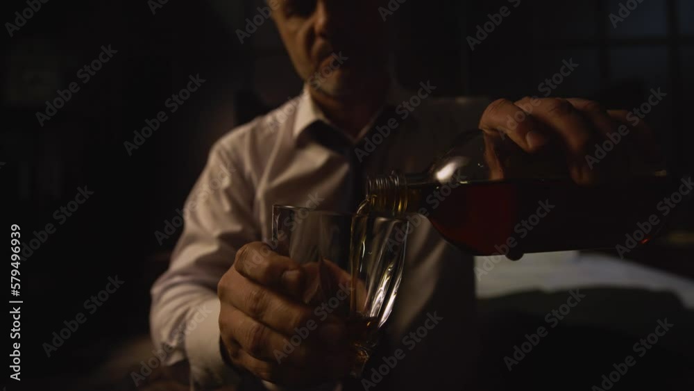 A close-up shot of a man in a white shirt and tie pouring alcohol from a decanter into a glass. Businessman drinks whiskey, scotch after a hard day, meeting, tired