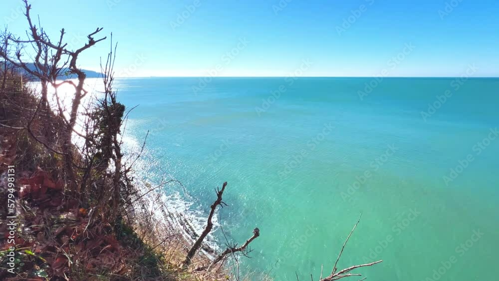 Panoramic view of the Black Sea coast from the mountain through the branches of trees. View of the blue water and the rocky seashore from the Kiselyov cliff. Sunset on the beach. 4K Panoramic view of the Black Sea coast from the mountain through the branches of trees. View of the blue water and the rocky seashore from the Kiselyov cliff. Sunset on the beach. 4K