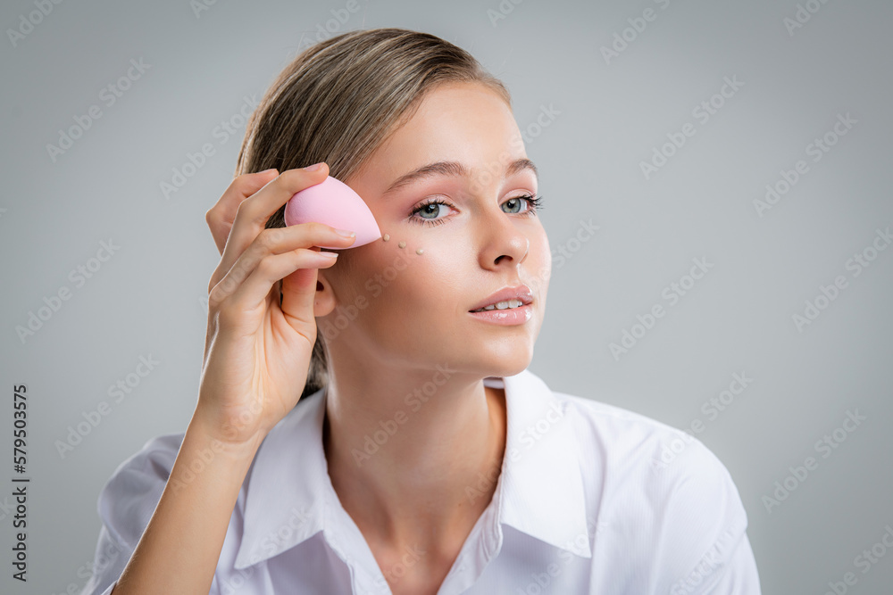 Cute beautiful natural brunette girl cleaning face with cotton sponge smiling looking at camera over white background. Cosmetology and spa.