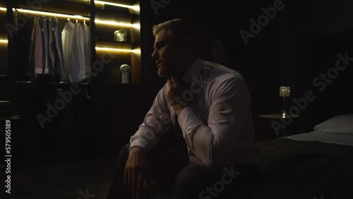 Businessman man in a suit came home sat on the bed, took off his jacket, tired, sighs, yawns, tired after working day, 