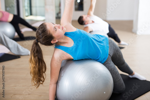 Young sporty woman doing exercises with pilates ball during group training at gym